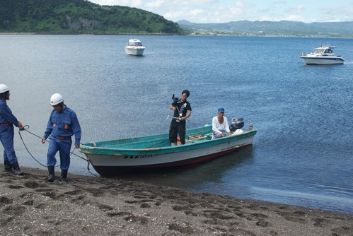 船で知林ヶ島に救助にきた一行を撮影する樋園撮影監督
